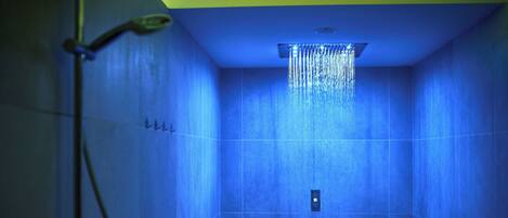 Un baño con paredes de azulejos azules, un cabezal de ducha y una tubería de agua a la vista.
