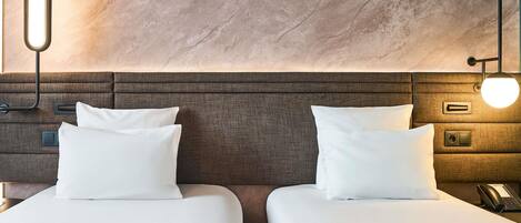 A hotel room with two beds, a wooden headboard, bedside lamps, a phone, and a wall-mounted light fixture.