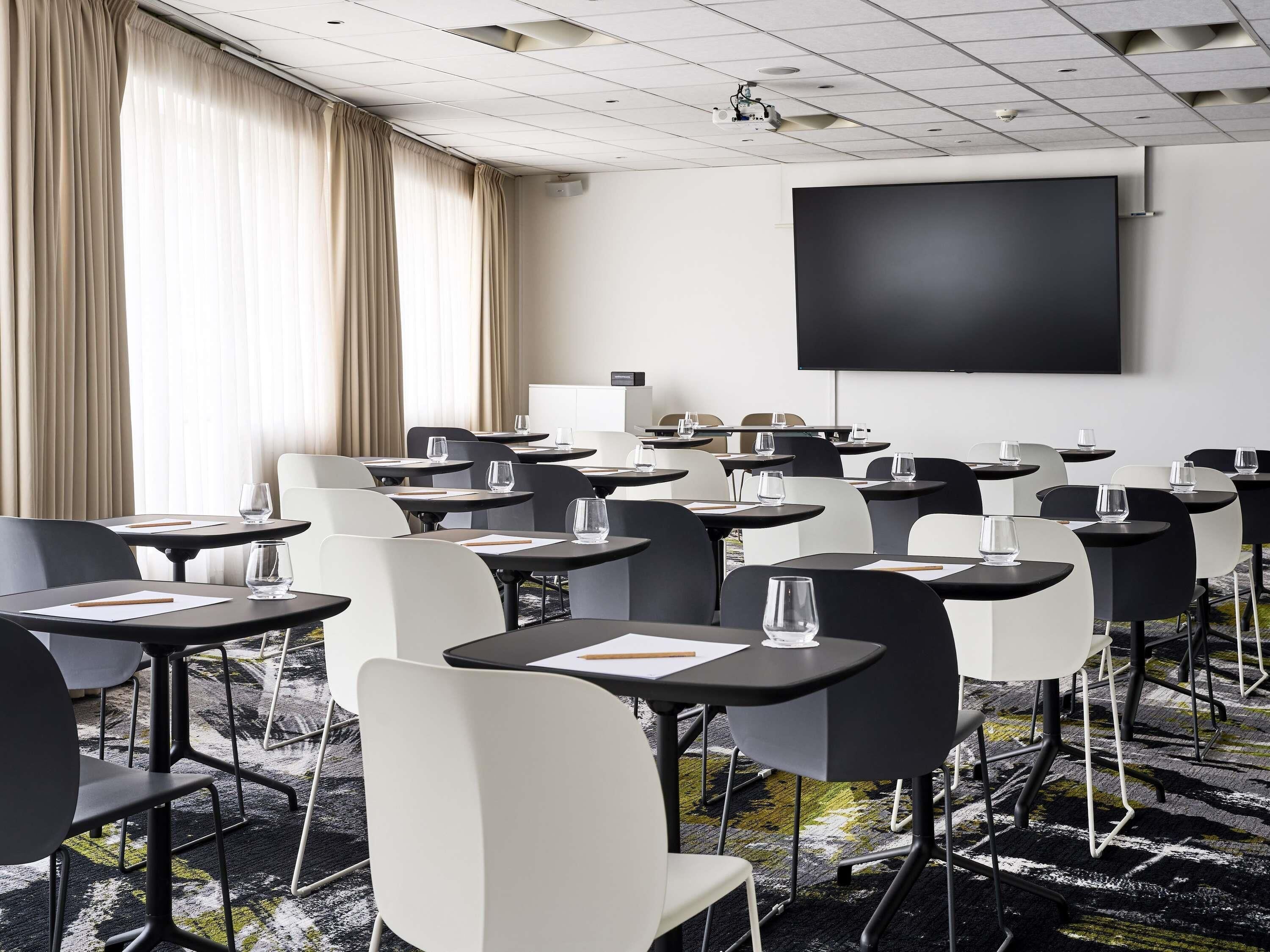 A conference room with tables, chairs, a projector, and a large screen.