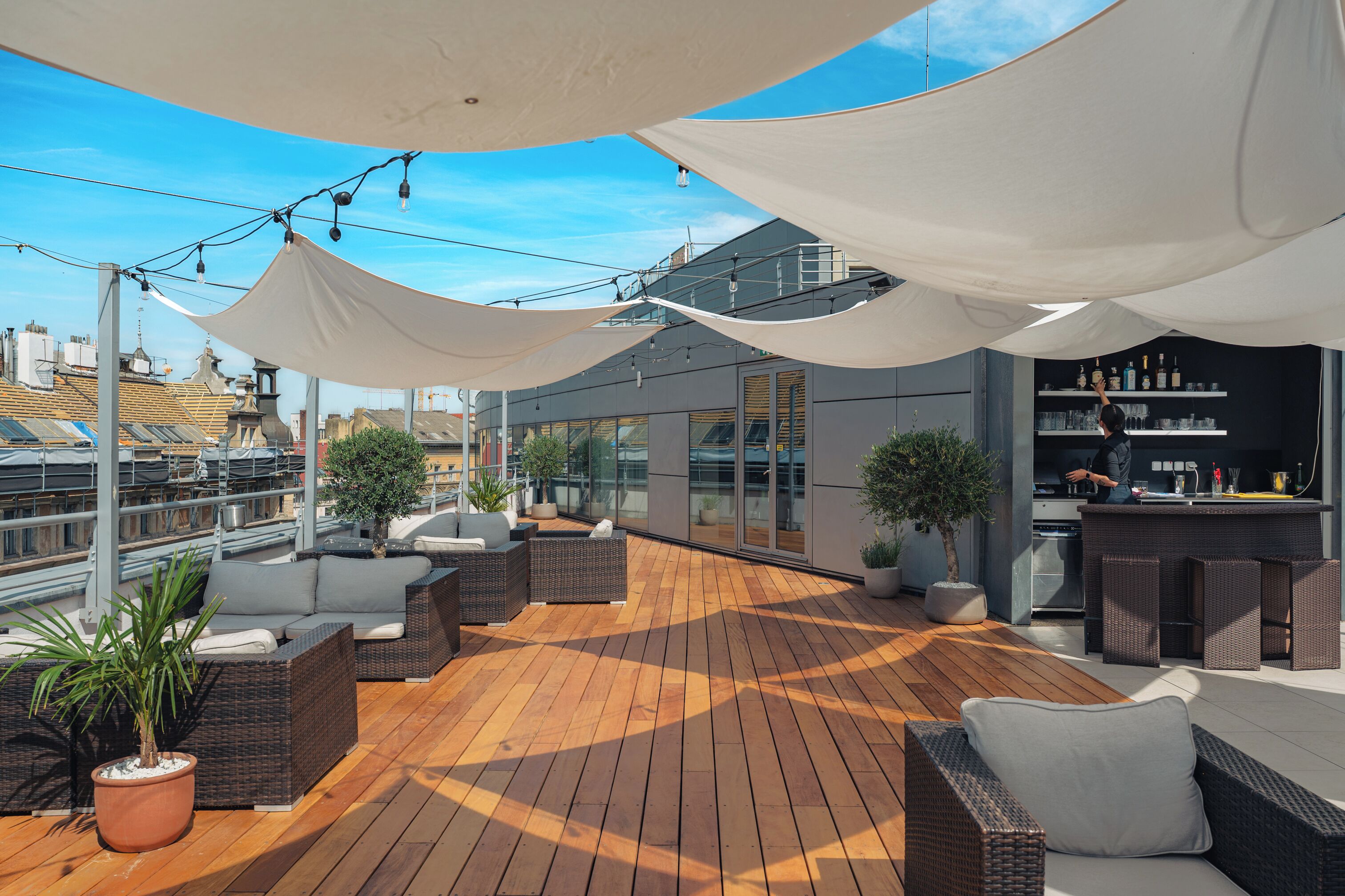Una terraza en la azotea con mobiliario exterior, zona de bar y vistas a la ciudad.