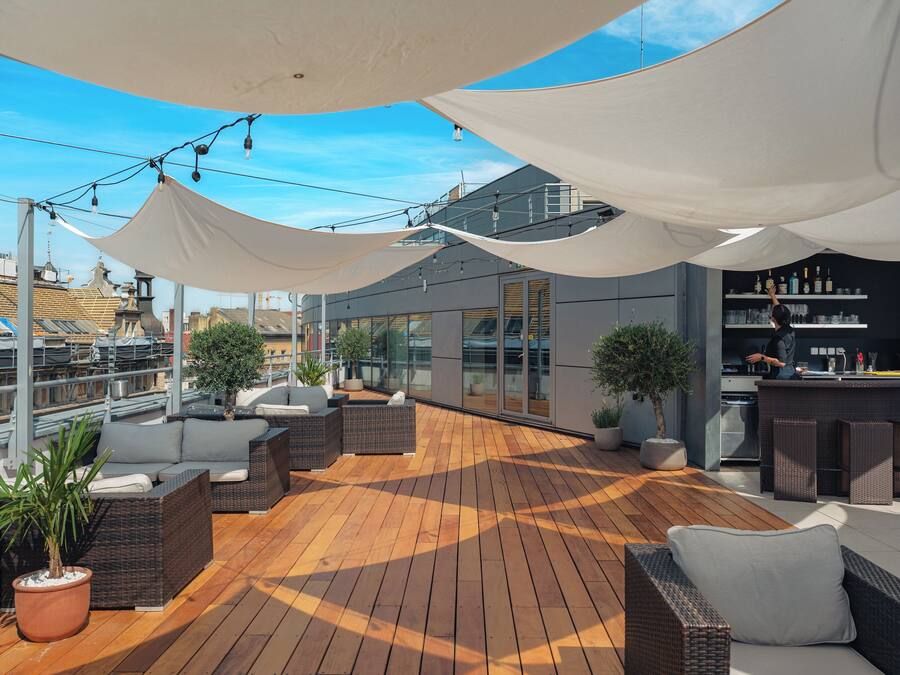 Una terraza en la azotea con mobiliario exterior, zona de bar y vistas a la ciudad.