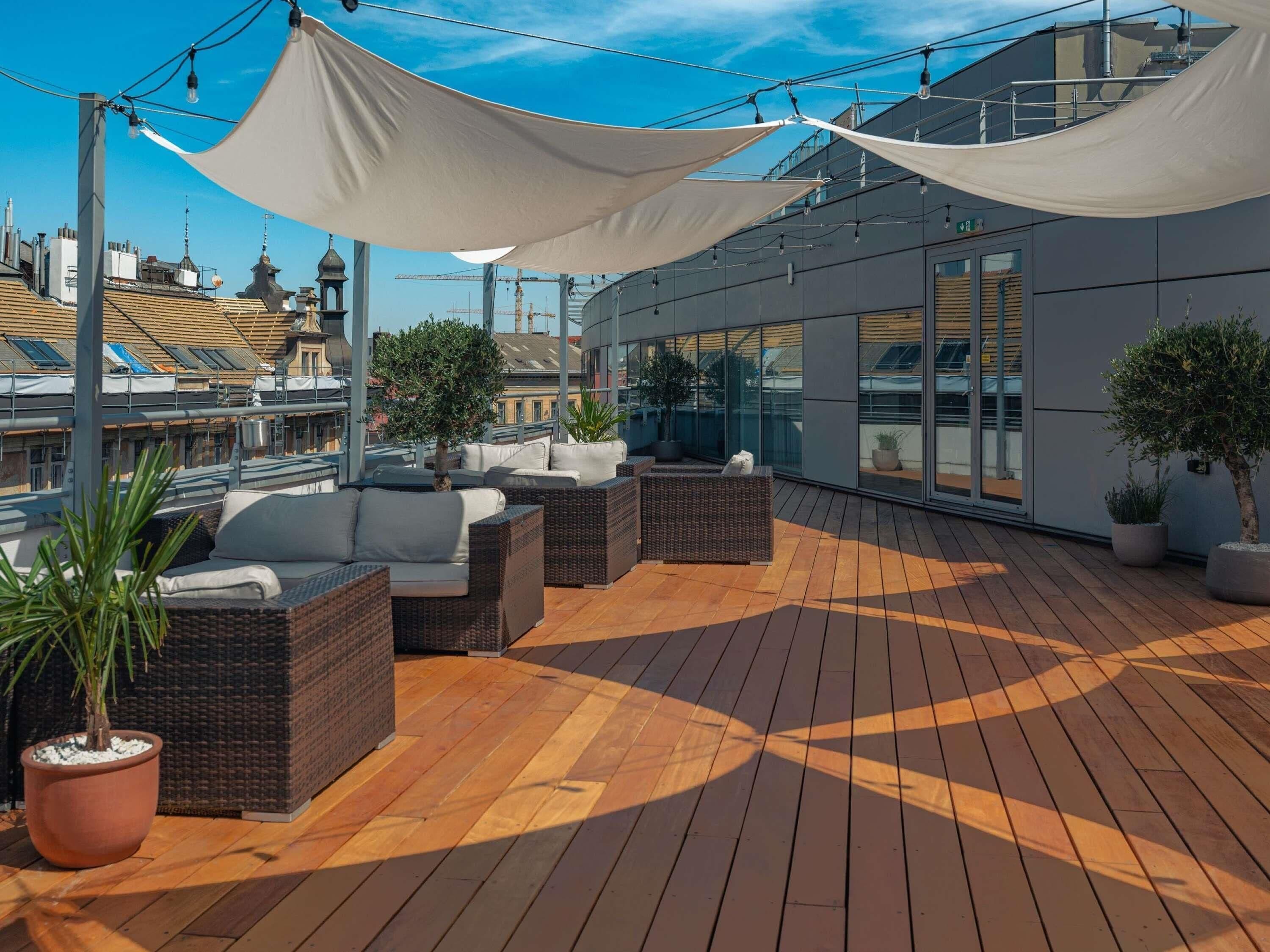 Una terraza en la azotea con mobiliario exterior, plantas en macetas y vistas de la ciudad.