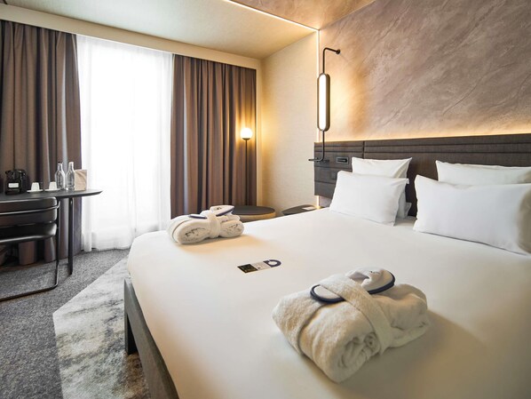 A hotel room with a neatly made bed, a desk with a coffee maker, and a wall-mounted light fixture. - Novotel Praha Wenceslas Square (Prague)