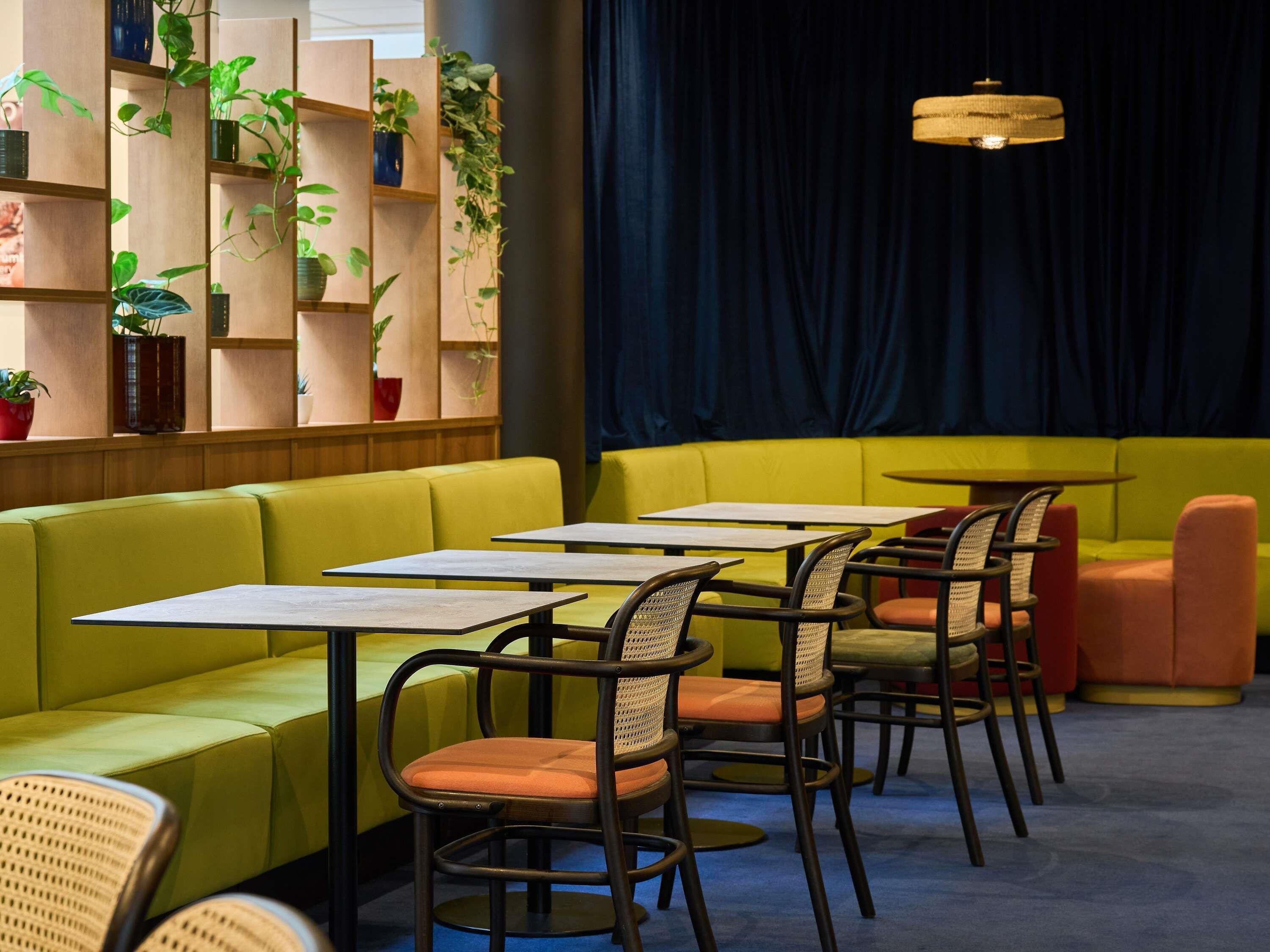 Interior de restaurante con zona de asientos en un banco amarillo, mesas, sillas de mimbre y un fondo de cortina oscura.