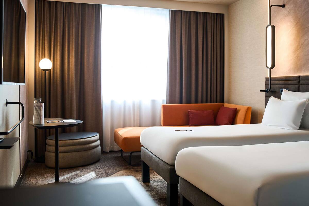 Une chambre d’hôtel avec un lit, un canapé, une petite table avec une lampe et une fenêtre avec des rideaux.