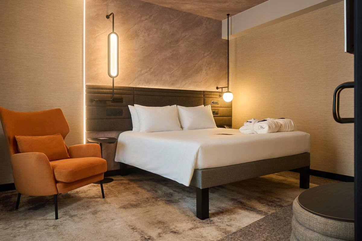 Une chambre d’hôtel moderne équipée d’un lit, d’une chaise, d’une table de chevet et d’une lampe.