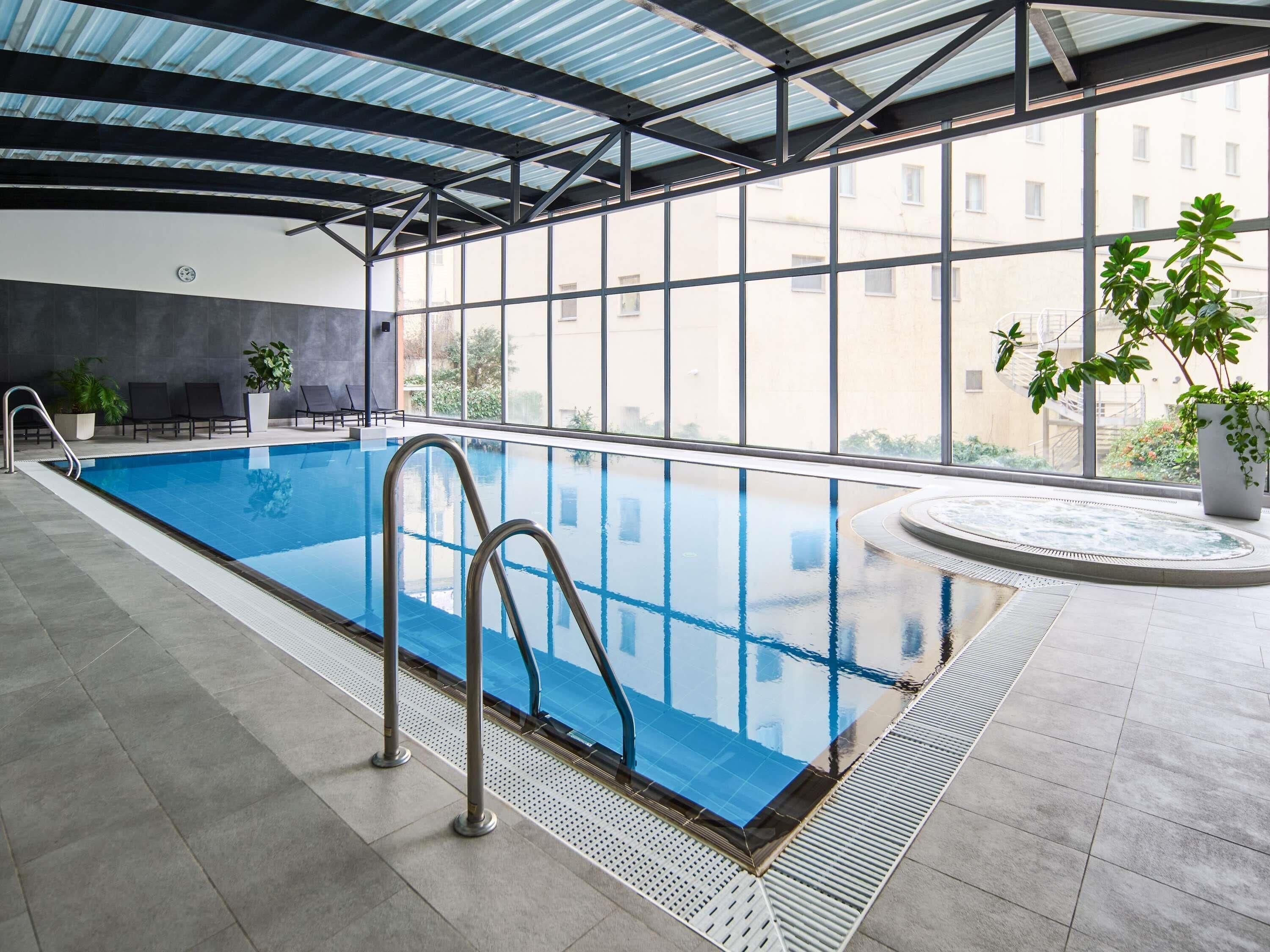 An indoor swimming pool with clear glass walls, a tiled floor, and a ceiling with a metal framework.