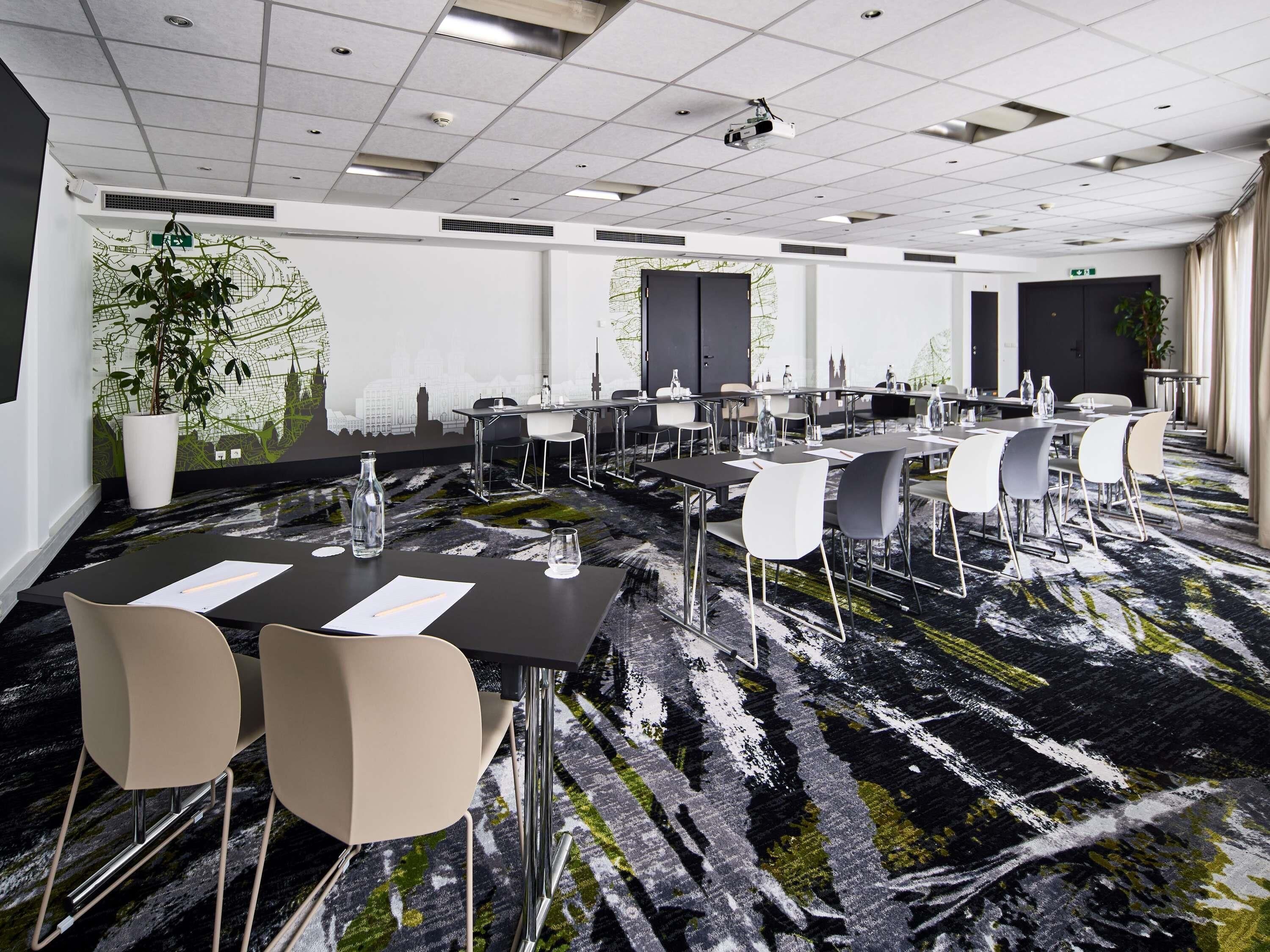 Una sala conferenze con una moquette a motivi bianco e nero, sedie bianche e grigie e un proiettore a soffitto.