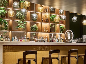 Zona de bar con varias lámparas esféricas colgantes, estantes con botellas y un cartel con espejo.