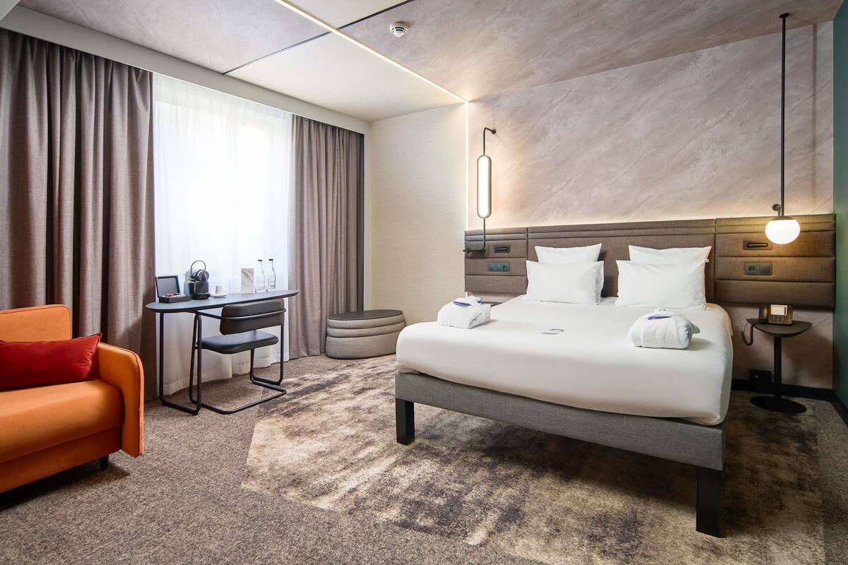 Une chambre d’hôtel comprenant un lit, un bureau, une chaise, un canapé et une table de chevet avec une lampe.