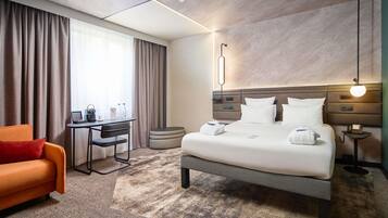 Ein Hotelzimmer mit Bett, Schreibtisch, Stuhl, Sofa und Nachttisch mit Lampe.
