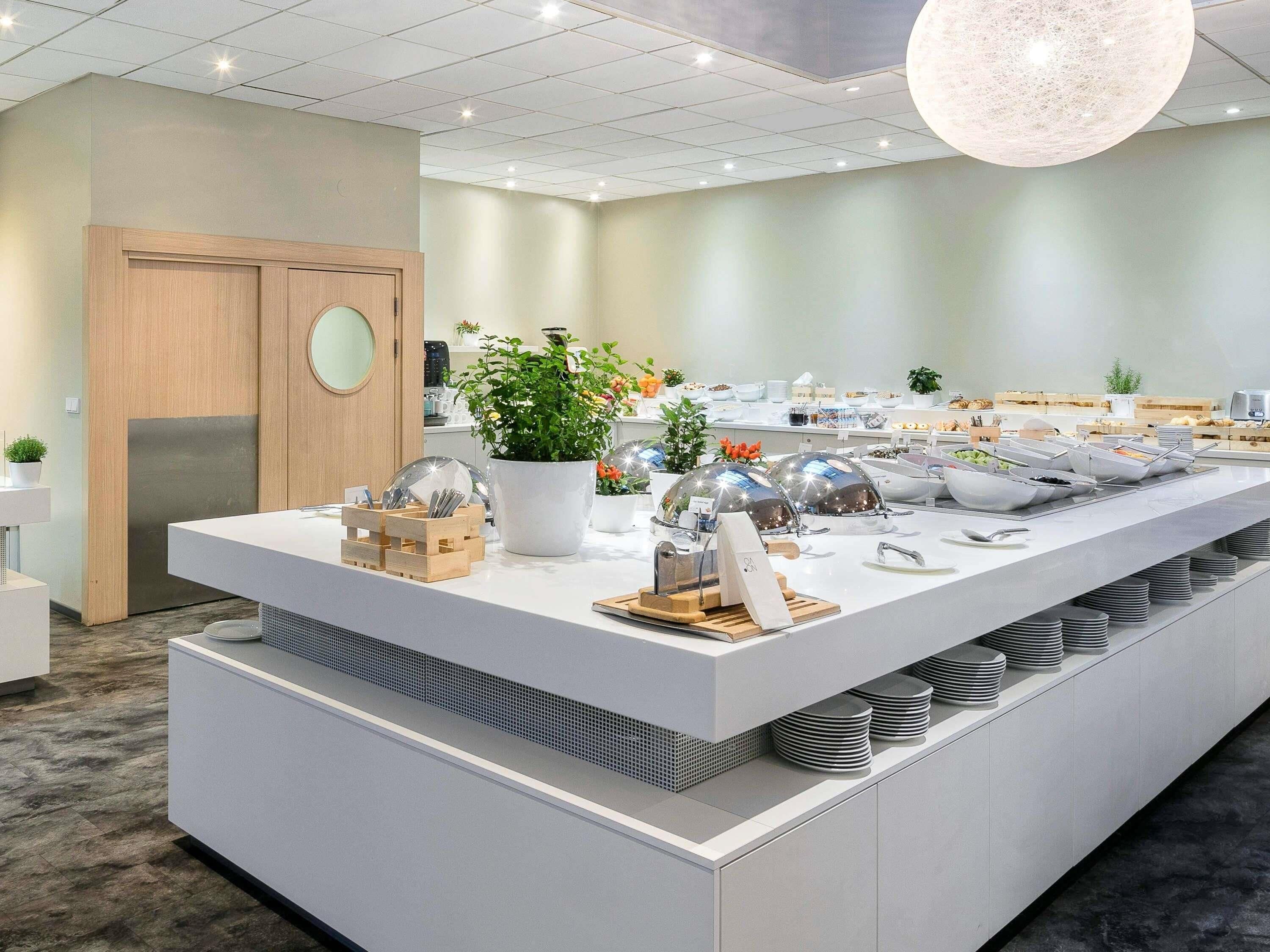 Uma zona de pequeno-almoço de hotel moderna, com uma ilha central, serviço de buffet e uma porta de madeira.