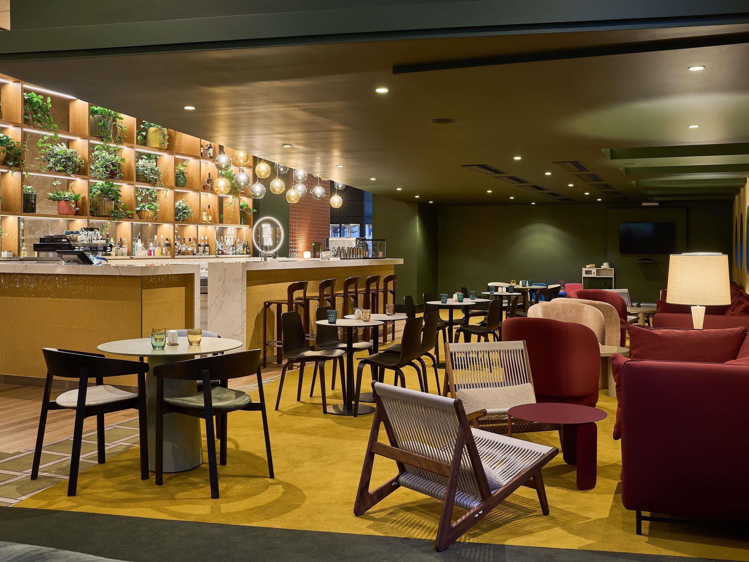 A modern bar area with a counter, seating, and a TV screen.