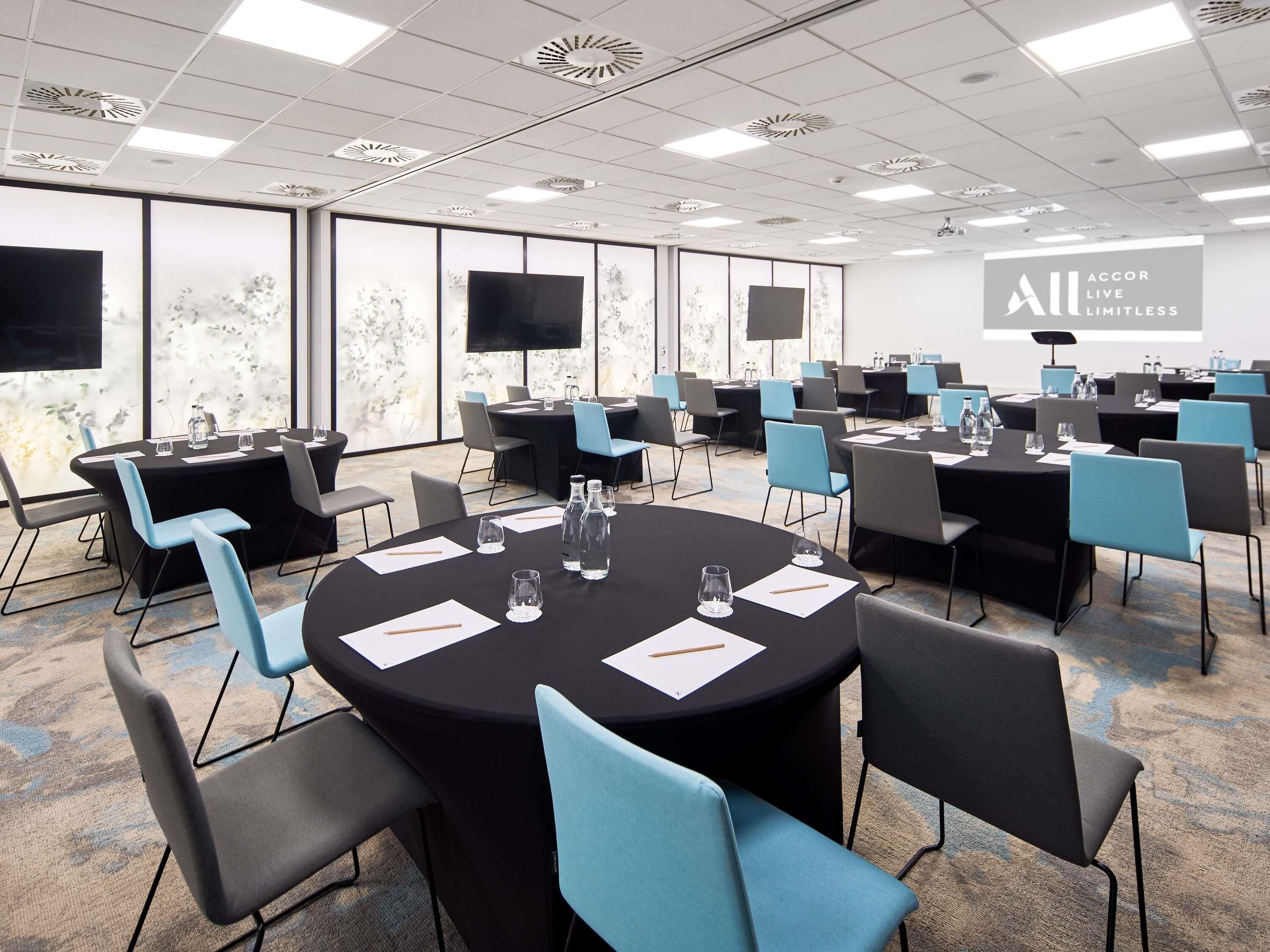 Un salón de conferencias con varias mesas, sillas y una pantalla grande.
