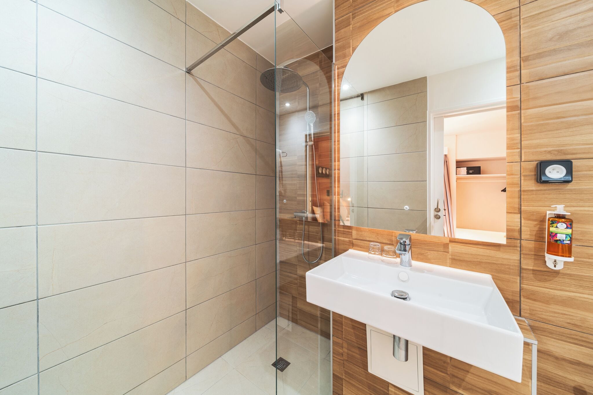 Un baño moderno con ducha envuelta en vidrio, lavamanos blanco y tocador de madera.