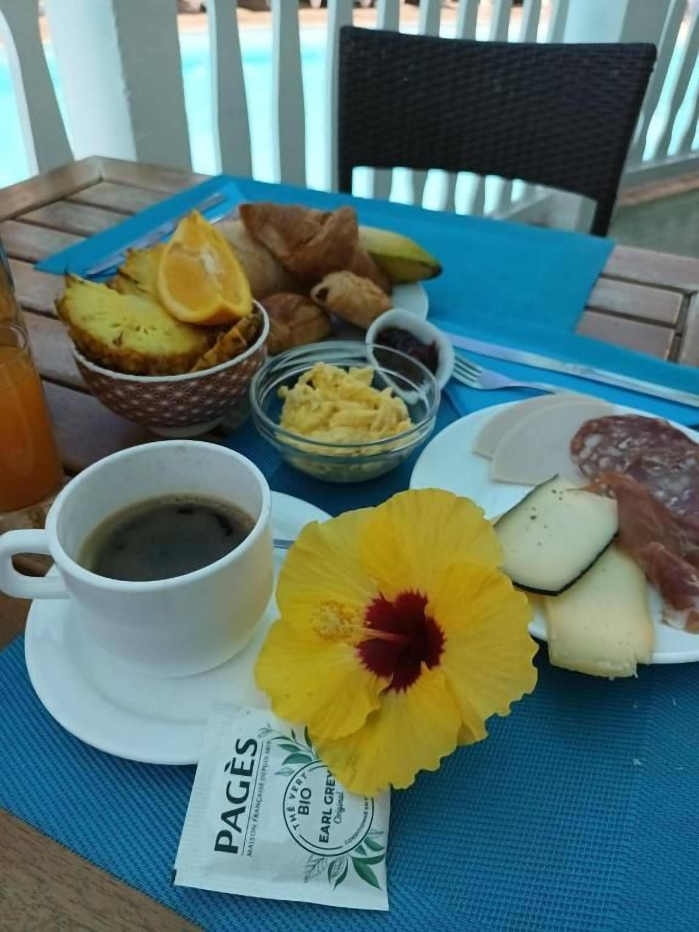 Une table dressée pour le petit-déjeuner, avec une tasse de café, des croissants, des fruits et un sachet de crème pour café.