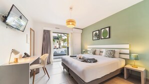 A modern hotel room with a bed, desk, chair, and a view of the outdoors. - Hôtel Exsel Ermitage (Saint-Paul)