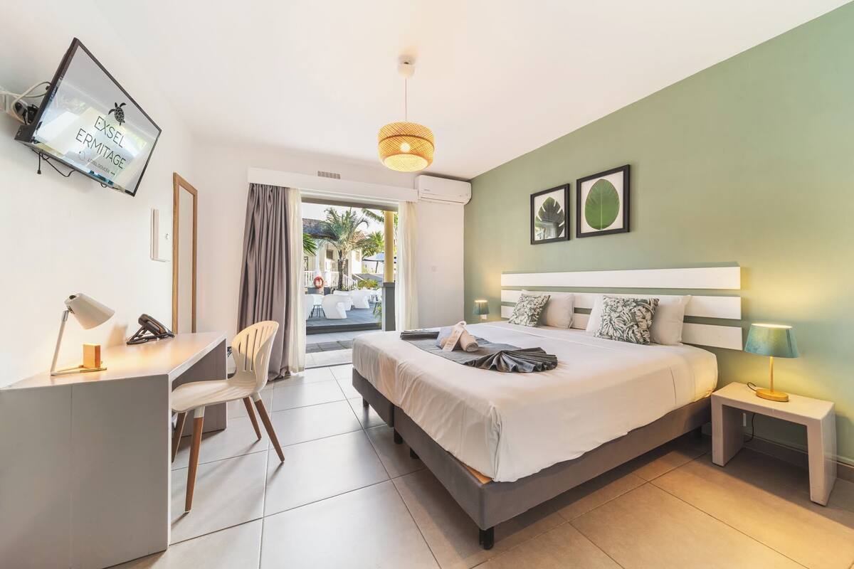 A hotel room with a bed, desk, chair, and a view of the outside.