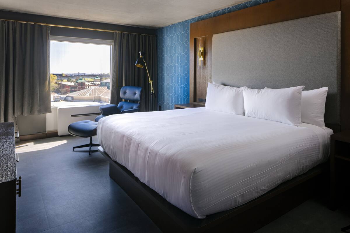 Habitación de hotel con una cama grande, un escritorio, una silla y una ventana con vistas a edificios.