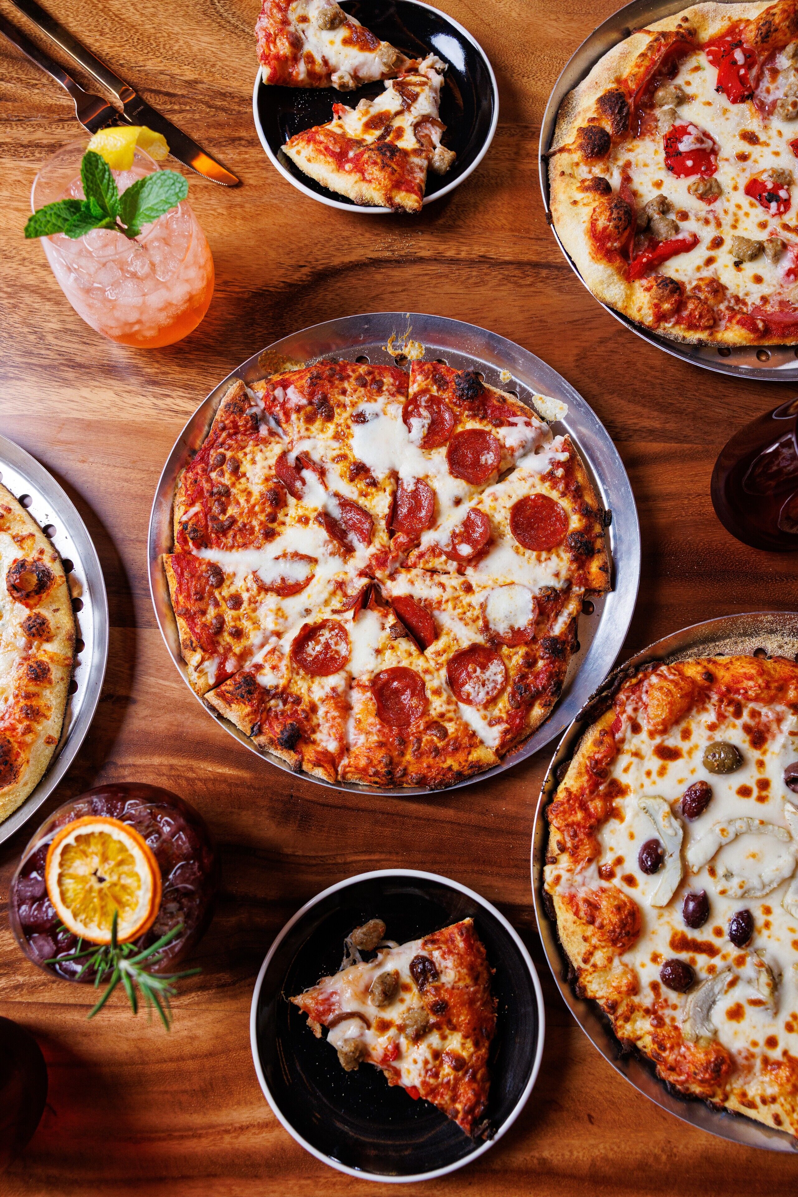 A pizza with pepperoni and cheese, a slice of pizza on a plate, and a drink with a lemon slice.