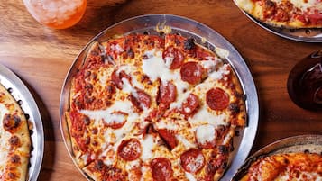A pizza with pepperoni and cheese, a slice of pizza on a plate, and a drink with a lemon slice.