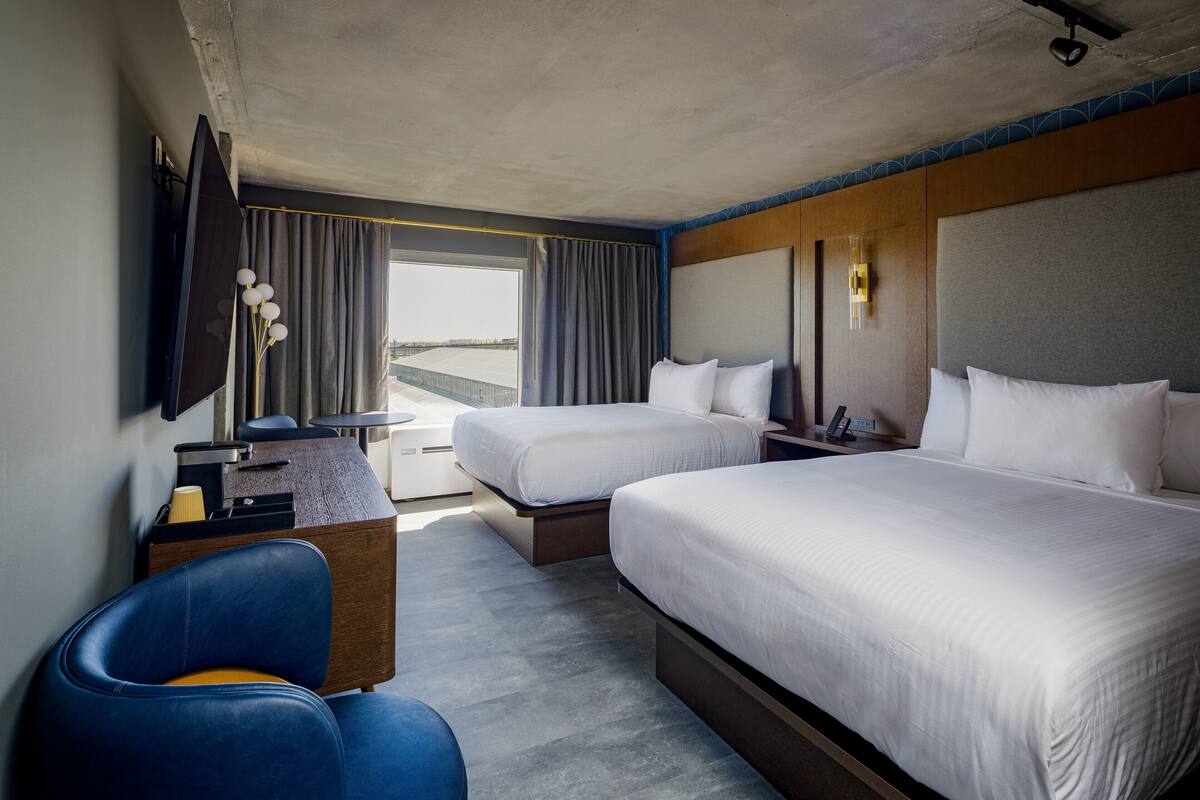 Habitación de hotel con dos camas, un escritorio, una silla y un televisor.