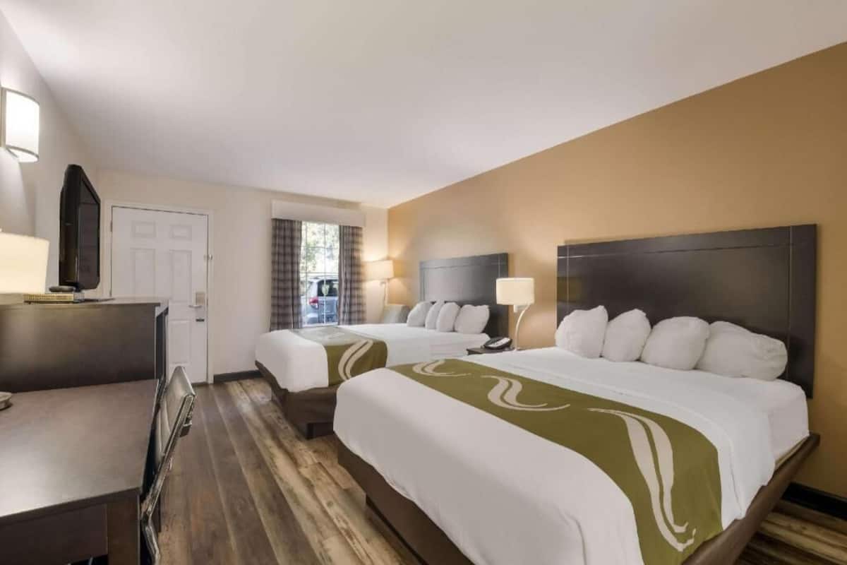 A hotel room with two beds, a desk, a chair, a TV, and a window with curtains.