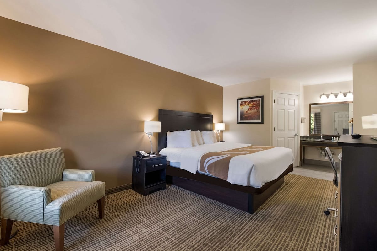 A hotel room with a bed, bedside table, lamp, chair, and a desk with a mirror.