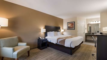 Ein Hotelzimmer mit Bett, Nachttisch, Lampe, Sessel und Schreibtisch mit Spiegel.