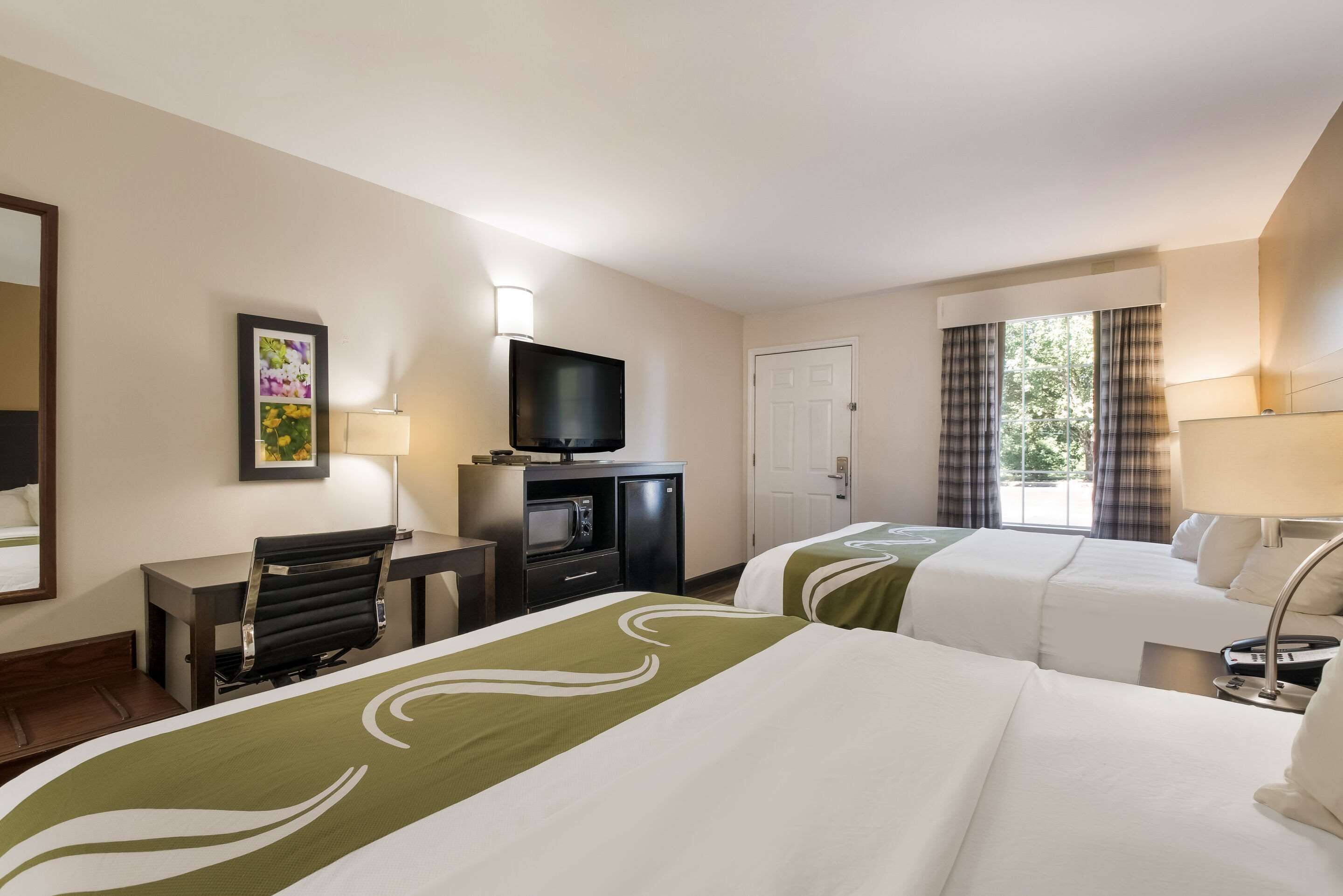 Habitación de hotel con dos camas, un escritorio, televisor y ventana con cortinas.