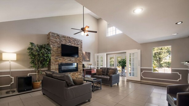 A spacious living room with a stone fireplace, comfortable seating, a flat-screen TV, and large windows offering natural light. - Quality Inn Decherd - Winchester (Decherd)