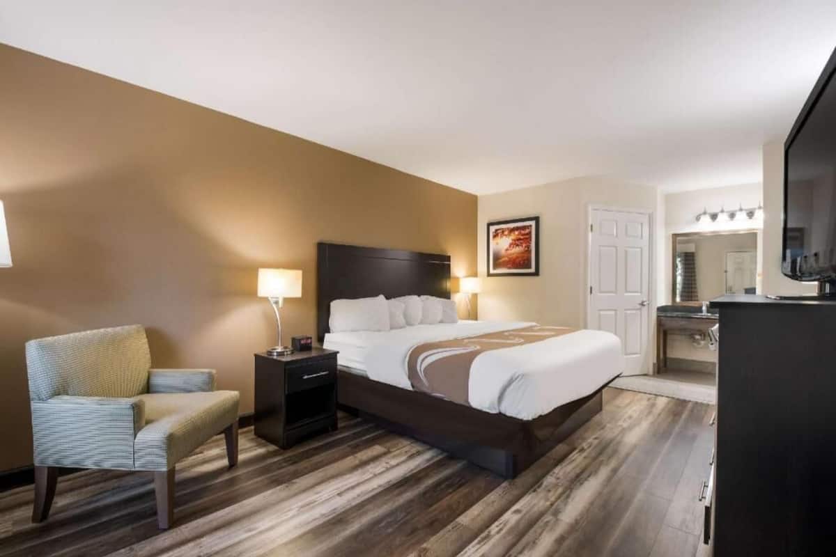 A hotel room with a bed, a chair, a nightstand, a desk, and a mirror.