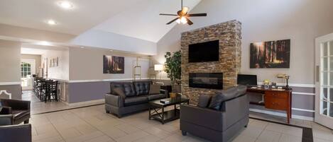 A spacious living room with a stone accent wall, a ceiling fan, and a flat-screen TV mounted above a fireplace.