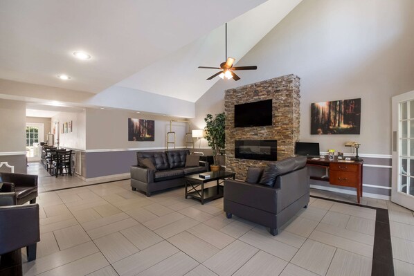 A spacious living room with a stone accent wall, a ceiling fan, and a flat-screen TV mounted above a fireplace.