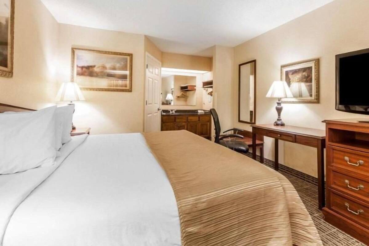 A hotel room with a bed, desk, chair, dresser, and television.