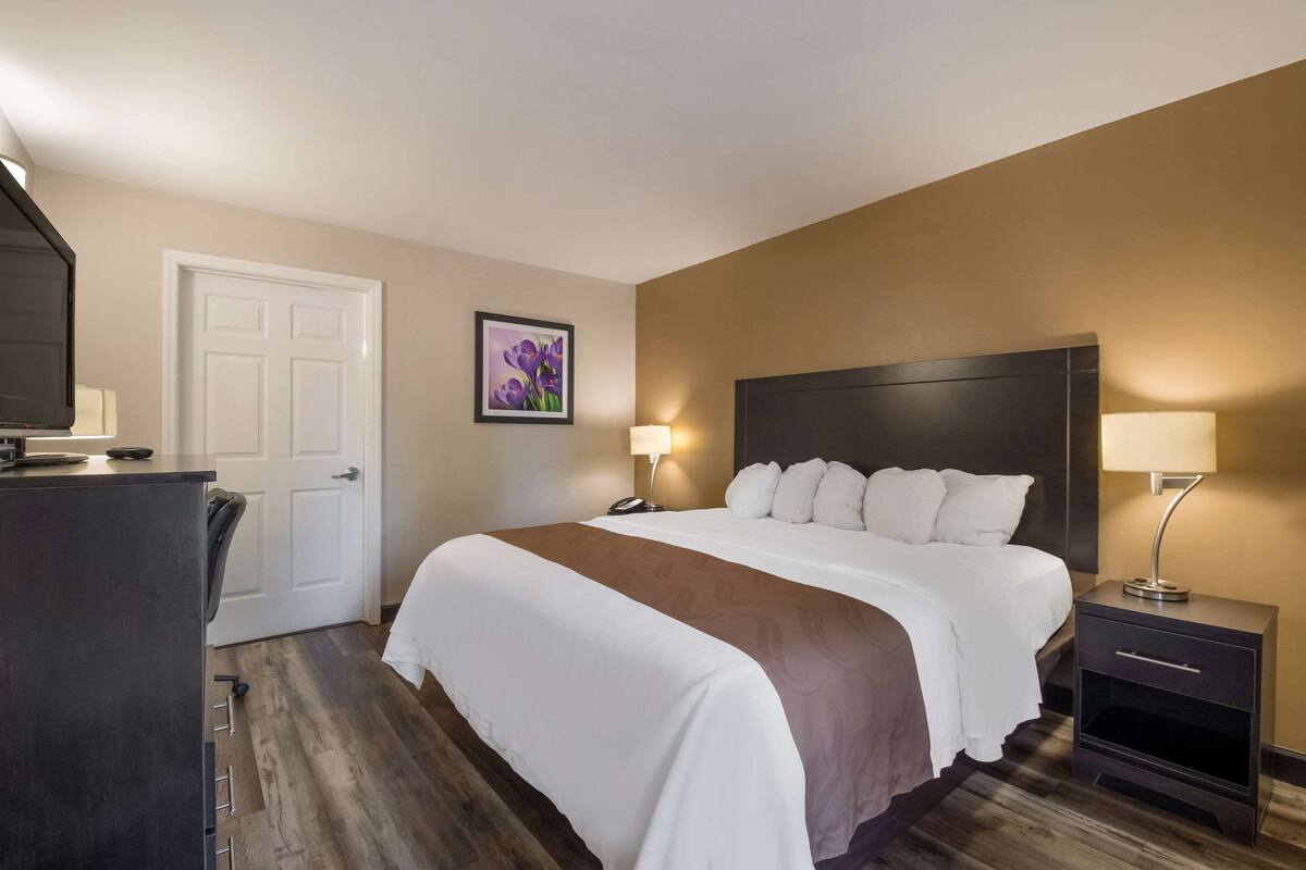 A hotel room with a large bed, bedside tables, a desk, and a door.