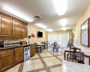 A kitchen with wooden cabinets, a refrigerator, a microwave, and a coffee maker. There are several chairs and a table. - Quality Inn Decherd - Winchester (Decherd)