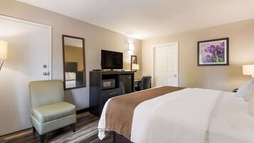 Une chambre d’hôtel avec un lit, un bureau avec une télévision, une chaise et une porte.