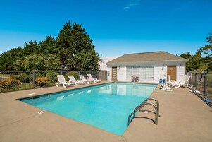 Una piscina rectangular con una escalera metálica, rodeada de sillas de descanso blancas y una zona delimitada por una valla.
