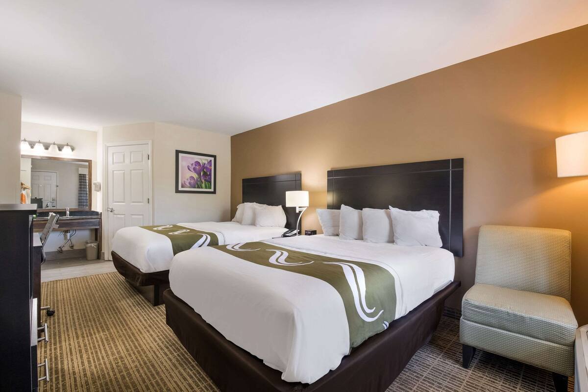 A hotel room with two beds, a desk with a mirror, a chair, and a wall-mounted lamp.
