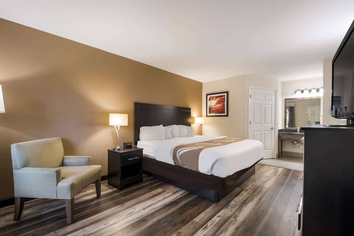 A hotel room with a bed, a chair, a nightstand, a desk, and a TV.