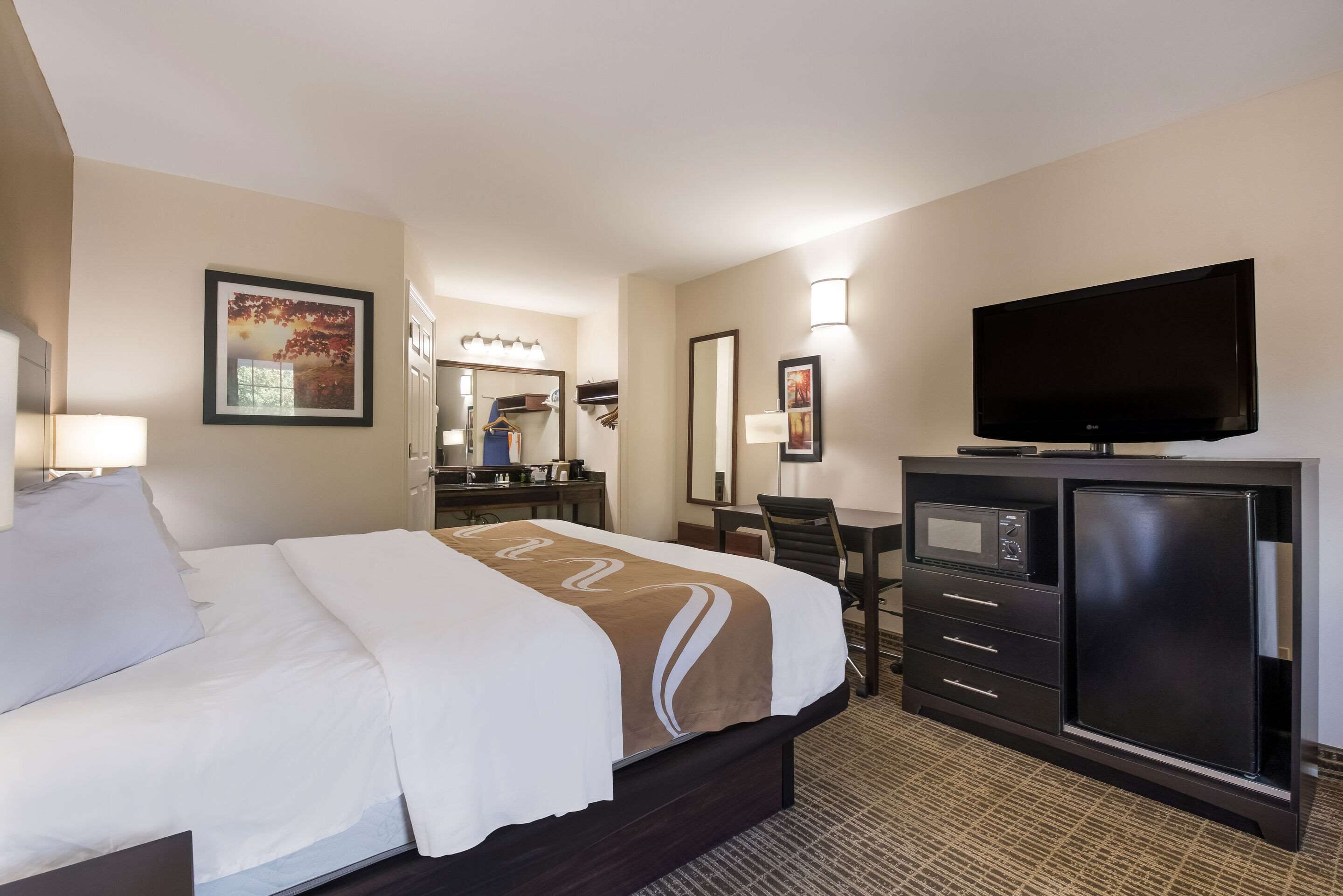 A hotel room with a bed, a desk with a computer, a television, and a microwave.