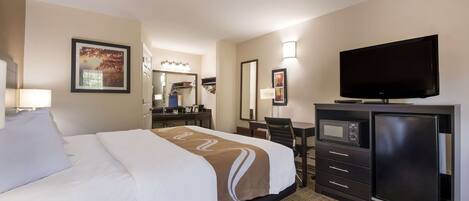 A hotel room with a bed, a desk with a computer, a television, and a microwave.