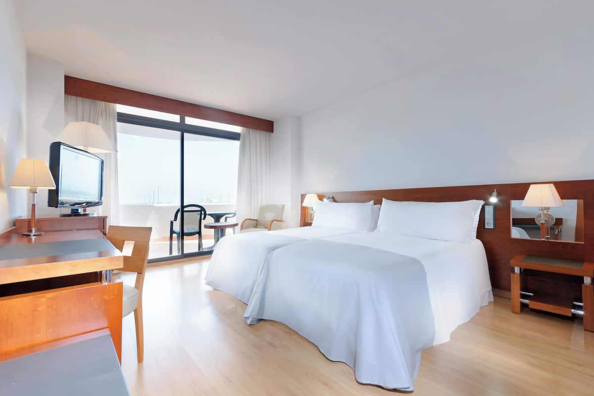 Ein Hotelzimmer mit einem großen Bett, einem Schreibtisch mit Stuhl, einem Fernseher und einem Fenster mit Vorhängen.