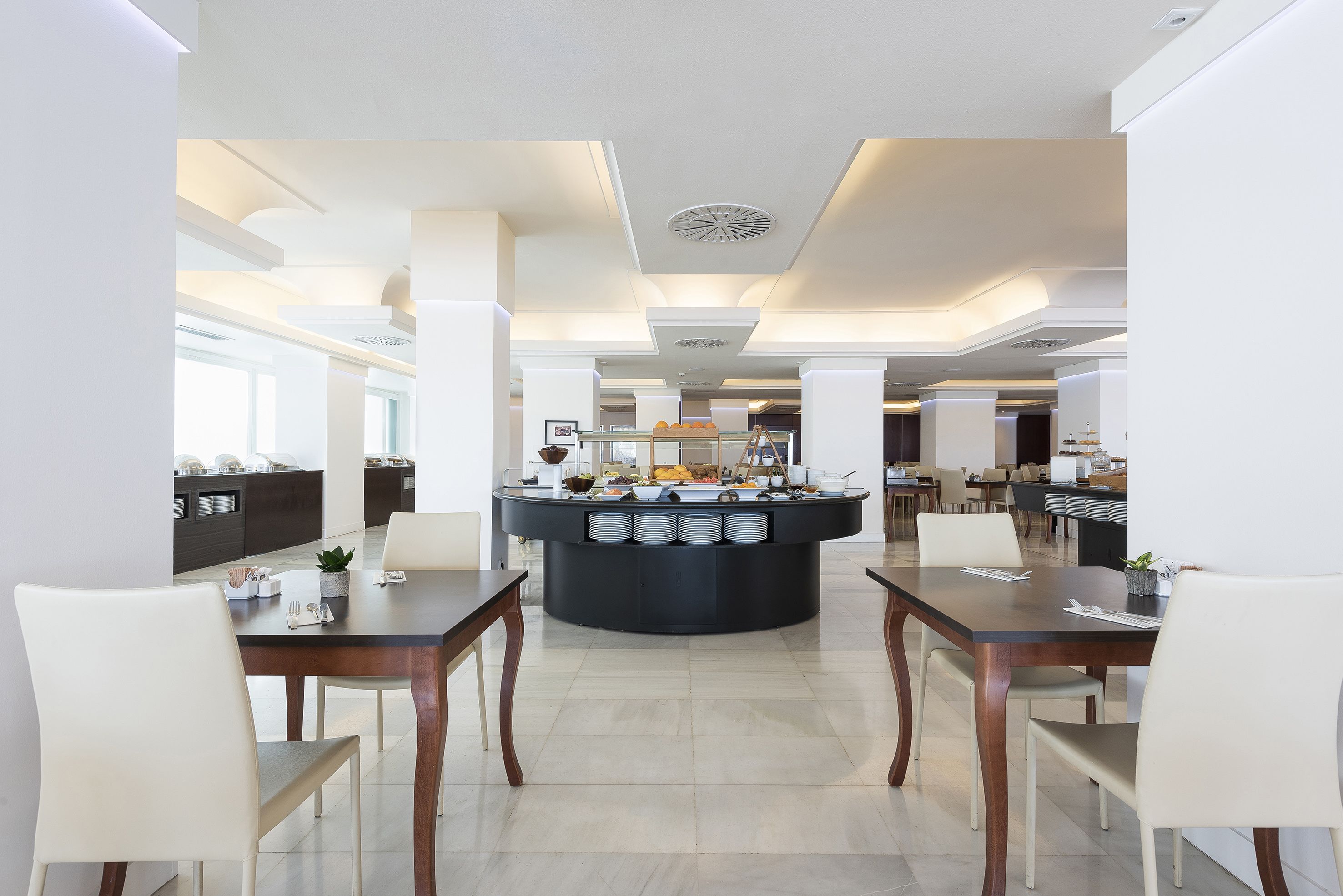 Un comedor moderno con un bufé central, sillas blancas y un diseño limpio y minimalista.