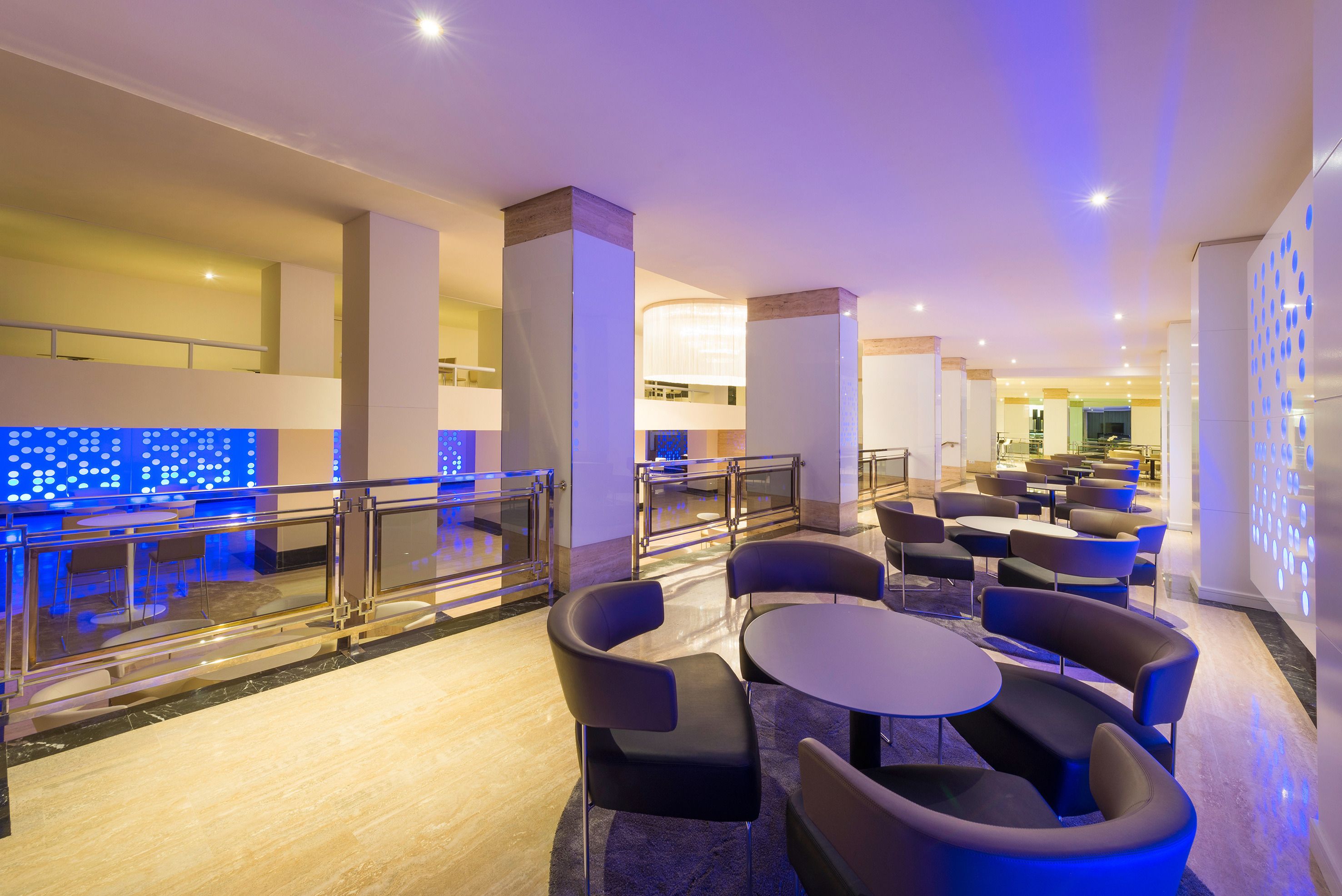 A modern hotel lobby with a seating area, glass railings, and a blue-lit wall.