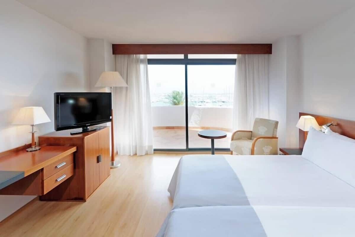 Ein Hotelzimmer mit Bett, Fernseher, Schreibtisch, Stuhl und einem Balkon mit Blick.