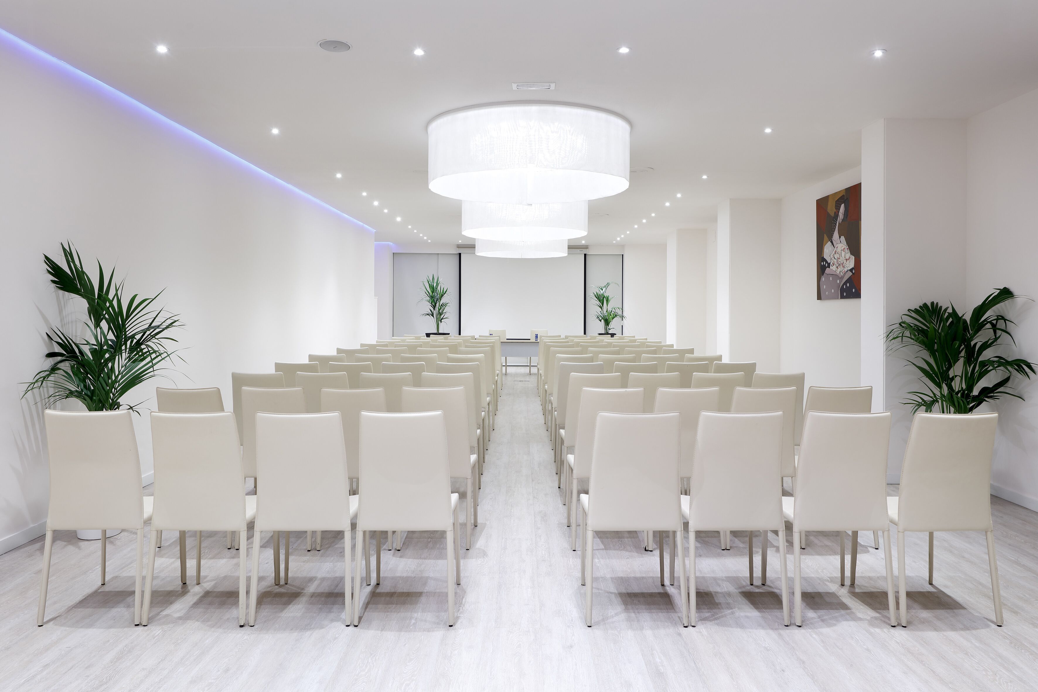 Une salle de conférence avec des rangées de chaises blanches, un grand lustre et des plantes en pot.