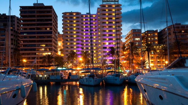 A marina with several boats docked, a hotel named 'HOTEL PALMA BEL VER' in the background, and a cityscape with buildings and palm trees. - Hotel Palma Bellver Affiliated by Meliá (Palma de Mallorca)