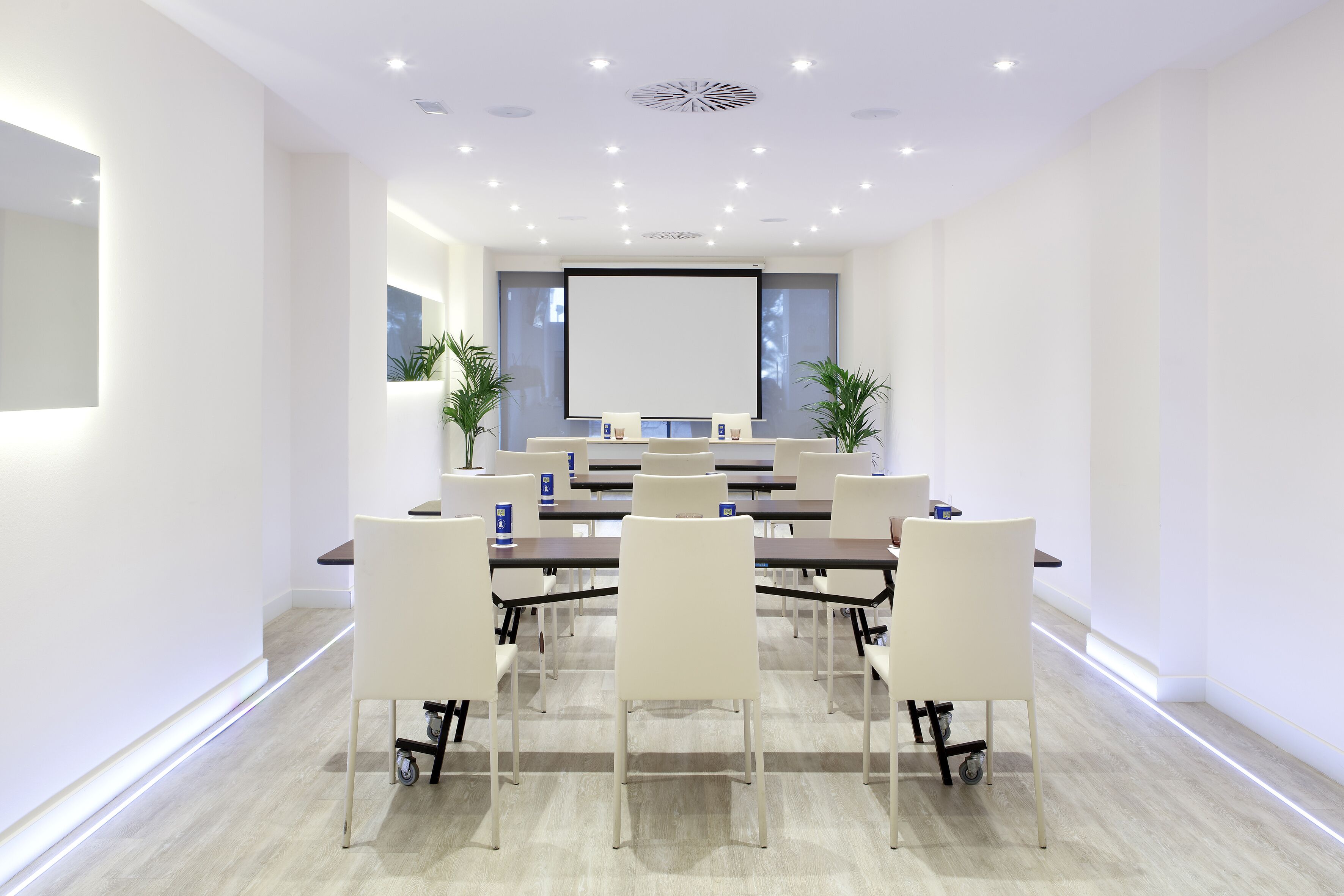 A modern conference room with a large screen, white chairs, and a long table.